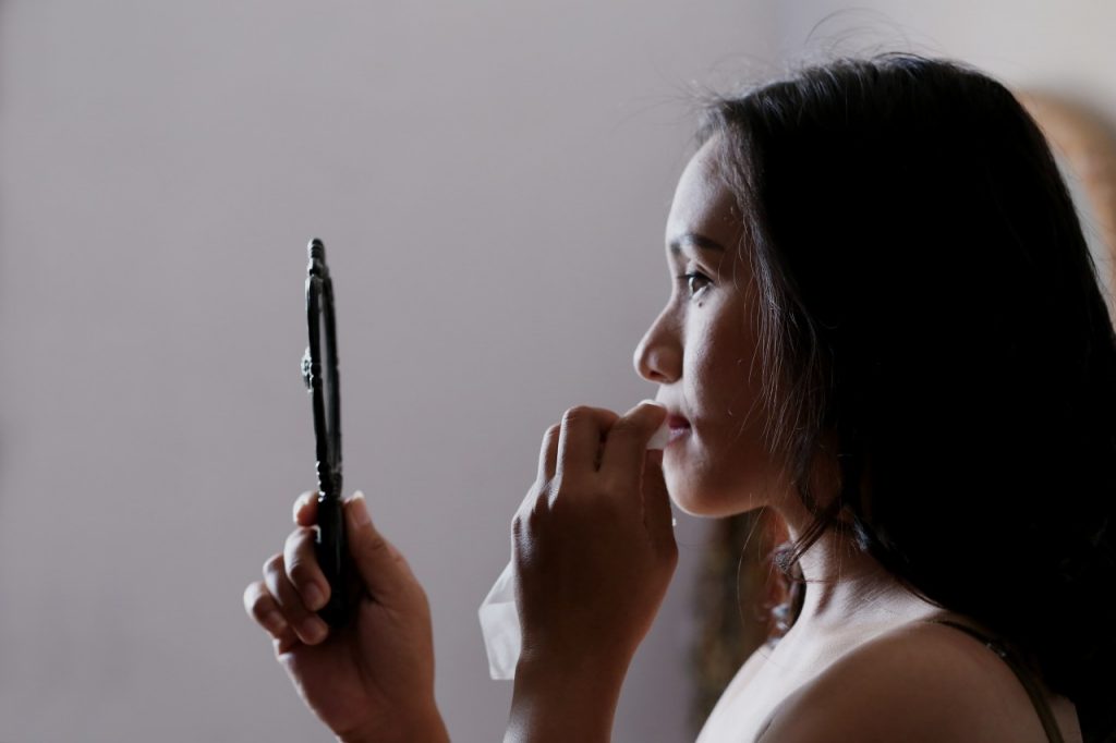 Woman looking in small hand mirror in profile