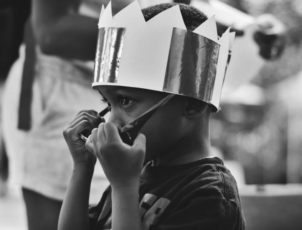Boy removing sunglasses and wearing a paper crown