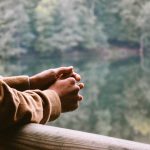 Man in brown coat waiting in front of water