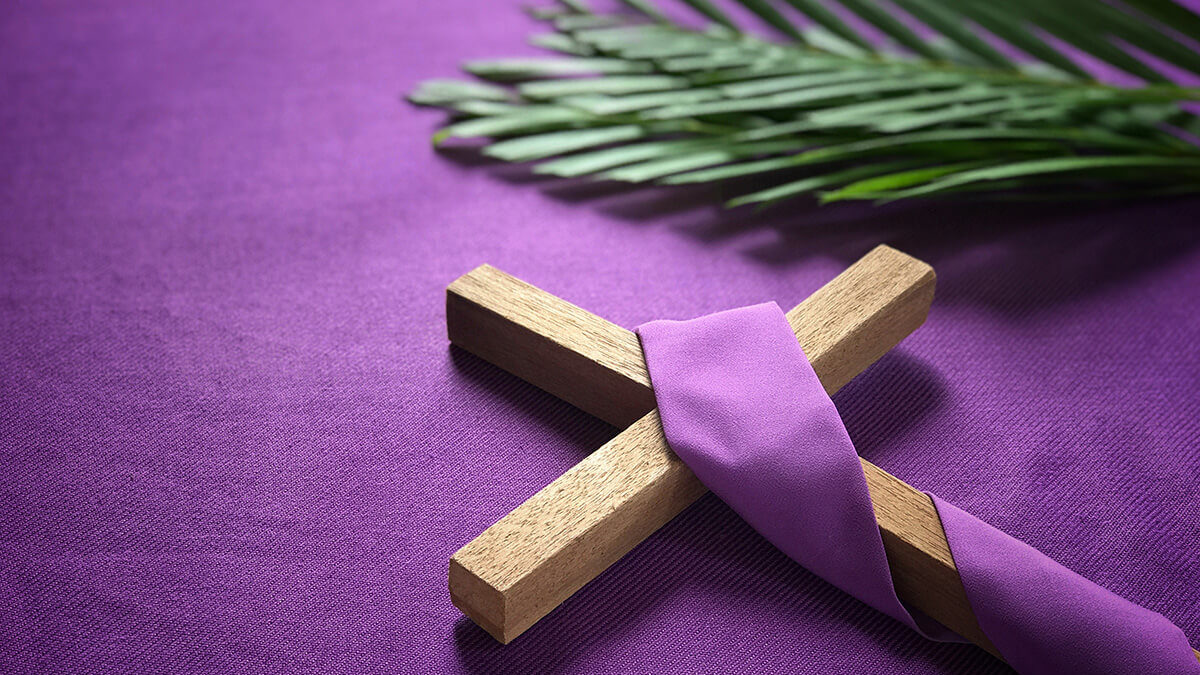 Wooden cross on purple tablecloth with palm